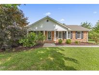 Charming brick home with manicured lawn, flowering bushes, and a covered front porch at 6411 Pondview Ln, Durham, NC 27712