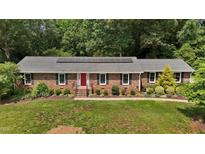 Charming brick ranch home with a red front door, lush landscaping, and solar panels at 825 Whispering Wind Rd, Burlington, NC 27217