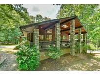 Stunning exterior elevation of a cabin-style home featuring stone pillars and a cozy porch area surrounded by lush trees at 110 Wolfs Trl, Chapel Hill, NC 27516