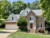 Beautiful two-story brick home boasts a well-manicured lawn and lush landscaping with mature trees at 122 N Fern Abbey Ln, Cary, NC 27518