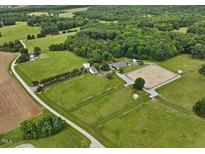 Picturesque aerial view of horse farm with fenced pastures and riding arena surrounded by lush greenery at 1624 Hopkins Rd, Bahama, NC 27503