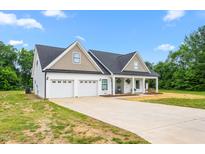 Charming home featuring a two-car garage, covered front porch, and a well-manicured lawn on a sunny day at 1711 Memory Ln, Burlington, NC 27217