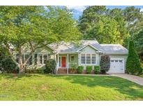 Charming one-story home with green siding, red door, lush lawn, mature trees, and an attached one-car garage at 5441 Millrace Trl, Raleigh, NC 27606