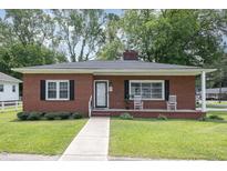 Charming single-story brick home featuring a manicured lawn, front porch with rocking chairs, and inviting curb appeal at 208 S College Ave, Kenly, NC 27542