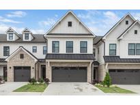 A modern townhouse with white siding, a gray brick facade, a dark garage door, and a well-manicured lawn at 109 Periwinkle Pl, Clayton, NC 27527
