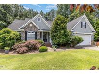 Charming home featuring stone accents, mature trees, and a lush, well-maintained lawn at 109 Jasmine Rose Ct, Holly Springs, NC 27540