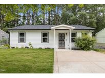 Charming white home with a well-manicured lawn and a cozy, inviting entrance with decorative door at 1204 Pecan Pl, Durham, NC 27704