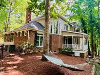 A beautiful home with a brick facade, large windows, and a covered porch, surrounded by lush greenery and a relaxing hammock at 1512 Cumberland Rd, Chapel Hill, NC 27514