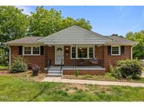 Charming brick home featuring a cozy front porch, complemented by a well-maintained lawn and mature trees at 305 Oakgrove Dr, Graham, NC 27253