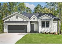Charming home showcasing vertical siding, a two-car garage, and a well-manicured lawn at 205 Shawnee Dr, Louisburg, NC 27549