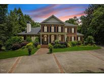 Elegant brick home with a manicured lawn, mature trees, and a circular driveway at sunset at 1009 Bentham Dr, Raleigh, NC 27614