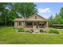 Charming brick home featuring a cozy front porch, landscaped garden, and a covered carport in the background at 3315 Mebane Oaks Rd, Mebane, NC 27302