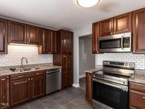 This kitchen features dark wood cabinetry, stainless appliances, granite countertops, and subway tile backsplash at 102 Sanair Ct, Apex, NC 27502
