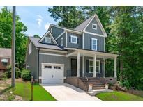 Charming two-story home featuring gray siding, a welcoming front porch, a well-manicured lawn, and a convenient attached garage at 415 1St St, Apex, NC 27502