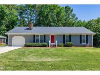 Charming single story home featuring a red front door, well-manicured lawn and mature trees at 100 Honeysuckle Ln, Cary, NC 27513