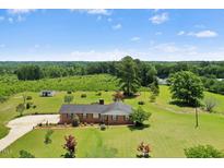 A ranch-style home with a brick facade, large front yard, mature trees, and a backdrop of lush greenery at 1035 Aquilla Rd, Benson, NC 27524
