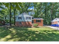 Charming two-story home with a brick base and light blue siding, surrounded by mature trees and a lush green lawn at 3221 Ward Rd, Raleigh, NC 27604
