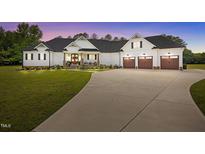 Charming white farmhouse-style home featuring a well-manicured lawn, covered porch, and a three-car garage at 2229 Neills Creek Rd, Lillington, NC 27546