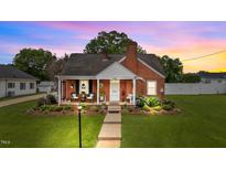 Charming brick home with a well-manicured lawn and cozy front porch at sunset at 9964 N Chestnut St, Middlesex, NC 27557