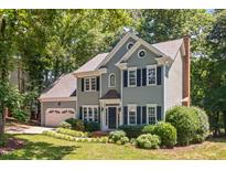 Charming two-story home featuring a well-manicured lawn, gray siding, and a brick chimney surrounded by lush trees at 5109 Windance Pl, Holly Springs, NC 27540