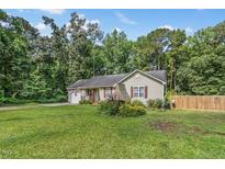 Charming single-story home with a well-maintained lawn, flower garden, and partial wooden fence under a blue sky at 229 White Oak Farm Dr, Willow Springs, NC 27592