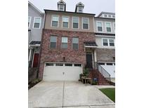 Charming townhome featuring a brick facade, a two-car garage, and a welcoming entrance with black metal handrails at 1005 Lathrop Ln, Apex, NC 27523