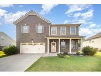 Two-story brick home featuring a well-maintained lawn, a two car garage, and a charming front porch at 1305 Ivey Grove Ct, Fuquay Varina, NC 27526