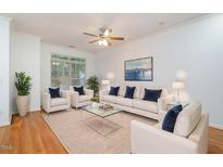 Bright living room features white sofa set, plush rug, ceiling fan, and natural light from a large window at 11710 Mezzanine Dr # 101, Raleigh, NC 27614