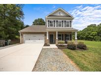 Charming two-story home featuring a brick facade, covered front porch, attached garage, and landscaped front yard at 2021 W Front St, Burlington, NC 27215