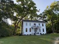 Charming two-story white home featuring a balcony and a well-manicured lawn surrounded by mature trees at 313 W Noble St, Louisburg, NC 27549