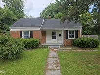 Charming brick home featuring a new roof, black shutters, landscaped yard, and inviting walkway to the front door at 704 N King Charles Rd, Raleigh, NC 27610