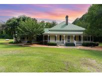 Charming home featuring a light yellow exterior, green metal roof, spacious porch, and lush landscaping with a stunning sunset backdrop at 6200 Us-401 S, Bunnlevel, NC 28323