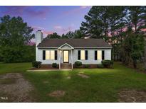 Charming white home with black shutters, a cozy front porch, and landscaped lawn beneath a beautiful sunset sky at 107 Winter Ct, Selma, NC 27576