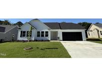 Charming one-story home with a well-manicured lawn, black garage door, and complementary landscaping at 128 Oakfield Trace Dr, Four Oaks, NC 27524