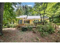 Charming yellow home with a wooden deck and lush landscaping surrounded by mature trees at 420 Lipscomb Grove Church Rd, Hillsborough, NC 27278