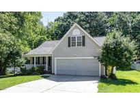 Charming home featuring a two-car garage and a cozy front porch, nestled among mature trees and lush greenery at 112 Avent Pines Ln, Holly Springs, NC 27540
