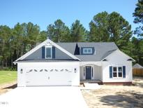 Charming white two-story home with a two-car garage and blue shutters is framed by lush trees under a clear blue sky at 776 Shadetree Rd, Benson, NC 27504