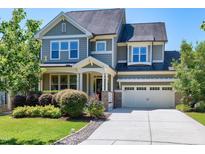 Charming two-story home with a manicured front yard and attached two-car garage on a sunny day at 129 Middlegreen Pl, Holly Springs, NC 27540