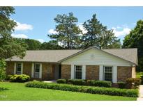 Charming brick ranch-style home with manicured lawn and mature trees under a blue sky at 1815 Chandellay Dr, Durham, NC 27705