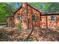 Cozy single-Gathering home featuring a brick chimney and brown siding, nestled amongst leafy trees at 5315 Mccormick Rd, Durham, NC 27713
