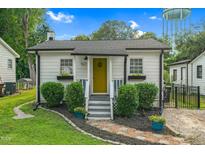 Inviting white cottage with a yellow door, complimented by green landscaping and a water tower at 527 N Cypress St, Wendell, NC 27591