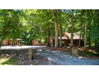 Charming log cabin nestled among mature trees with a gravel driveway and multiple outbuildings at 3263 S Jim Minor Rd Rd, Haw River, NC 27258