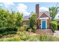 Charming brick home with a beautiful, lush front garden and a vibrant blue front door at 1007 W Markham Ave, Durham, NC 27701