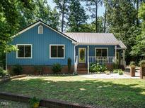 Charming home with blue siding, metal roof, white porch and landscaped yard surrounded by mature trees at 1487 Kentucky Ave, Sanford, NC 27332