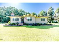 Charming ranch style home with well-manicured lawn, mature trees, and an American flag on the front porch at 233 Pressly Foushee Rd, Sanford, NC 27330