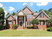 Beautiful two-story brick home with manicured lawn, mature trees, and classic architectural detailing at 312 Flint Point Ln, Holly Springs, NC 27540