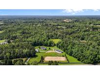 Expansive aerial view of horse property featuring a home, stable, and riding arena surrounded by lush greenery and wooded areas at 3511 Corbett Rd, Mebane, NC 27302