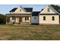 Charming white farmhouse-style home featuring a welcoming front porch with stylish black railings and brick accents at 50 Leah Ln, Louisburg, NC 27549