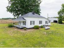 Charming white farmhouse with a metal roof and a spacious front yard surrounded by mature trees at 5004 Us 70 Alt, Princeton, NC 27569