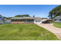Charming brick home featuring a manicured lawn, attached garage, and a convenient carport on a sunny day at 117 James Dr, Pine Level, NC 27568
